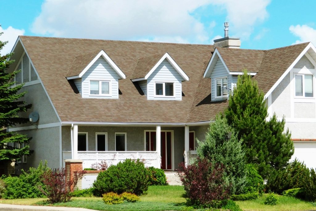 Gray craftsman style home with dormer windows, a covered front porch, and landscaped shrubs